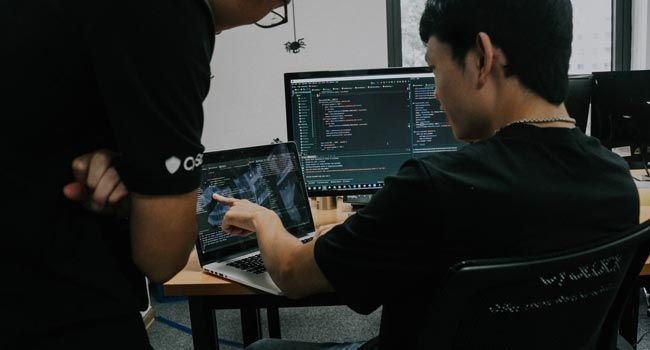 Zwei Personen schauen sich eine Programmiersprache auf einem Laptopbildschirm an. 