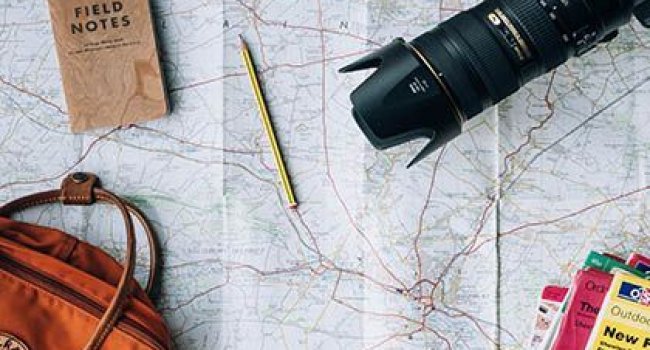 Das Foto zeigt Reisevorbereitungen mit einer Landkarte, Tasche und einem Fotoapparat.