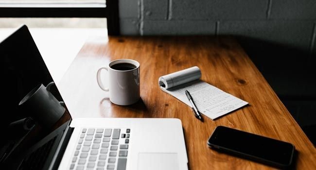Laptop, Smartphone, Schreibblock und ein Kaffee auf einem Schreibtisch