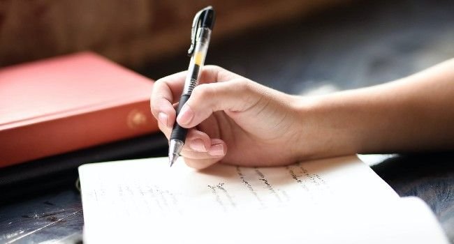 Hand einer Person schreibt in ein Buch.