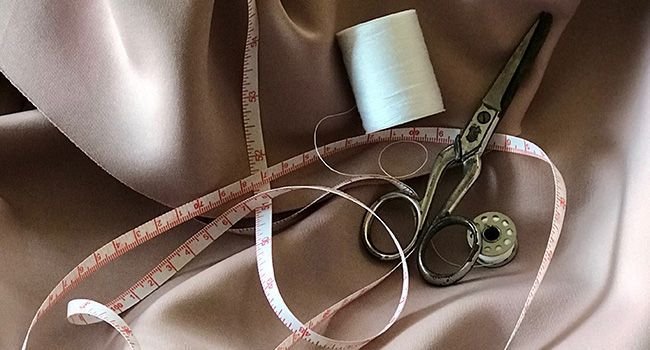 Zollband, Fadenrolle und Schere auf beige farbenem Stoff