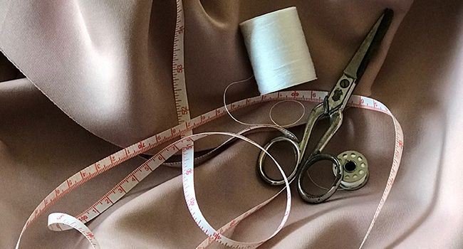 Zollband, Fadenrolle und Schere auf beige farbenem Stoff