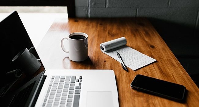 Ein digitaler Arbeitsplatz mit einem Laptop, Smartphone und einer Tasse Kaffee daneben
