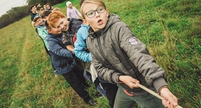Kinder im freien auf einer Wiese beim Tauziehen.