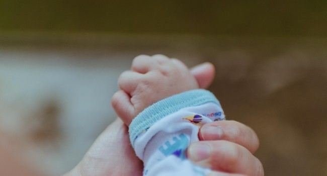 Person hält die Hand eines Kleinstkindes.