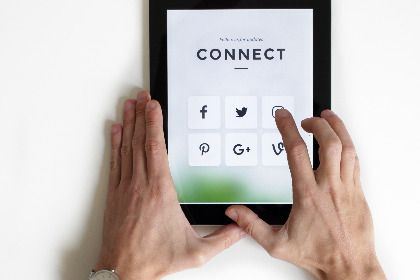 Photo by NordWood Themes Zwei Hände halten ein Tablet, auf dem Social Media Icons zu sehen sind.
