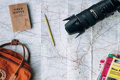Photo by Annie Spratt on Unsplash Das Foto zeigt Reisevorbereitungen mit einer Landkarte, Tasche und einem Fotoapparat.